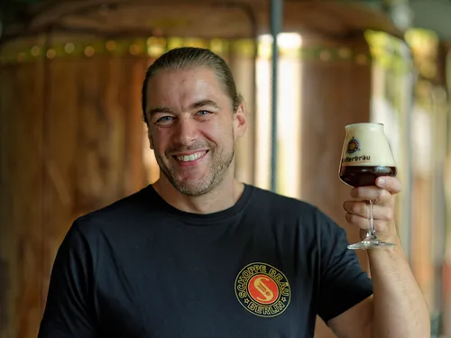 Man lifts a glass of beer in a brewery.