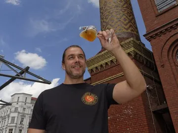 Mann hält ein Glas Bier vor einer Ziegelfabrik.