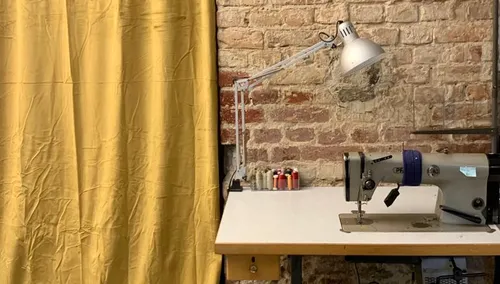 Nähmaschine auf Tisch unter einer Lampe, umgeben von Stoff.