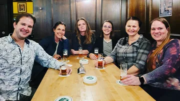 Sechs Personen sitzen gemeinsam an einem Tisch mit Bier.