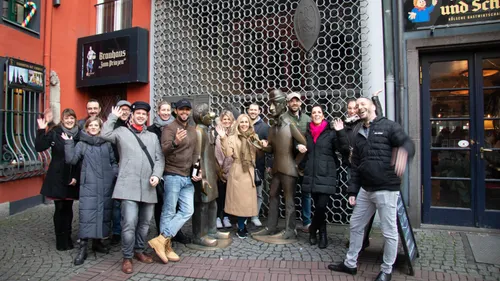 Gruppe von Menschen winkt vor bronzenen Statuen in Stadt.