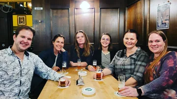 Six people sit at the table and drink beer.