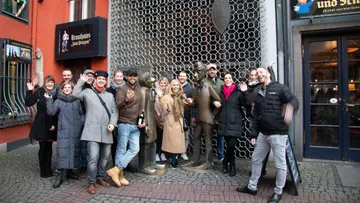 Group of people wave next to two statues in the city.