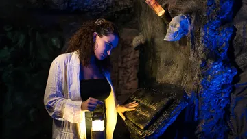 A woman uses a lamp to illuminate a blackboard in a cave.