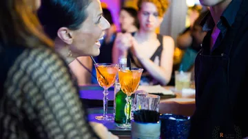 Zwei Cocktails stehen auf der Theke, während Leute plaudern.