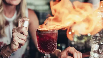 Brennender Cocktail wird mit Spray in einer Bar angezündet.