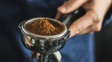 Hand holds a portafilter with ground coffee.