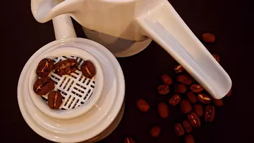 Weiße Kaffeekanne mit Bohnen auf einem dunklen Tisch.