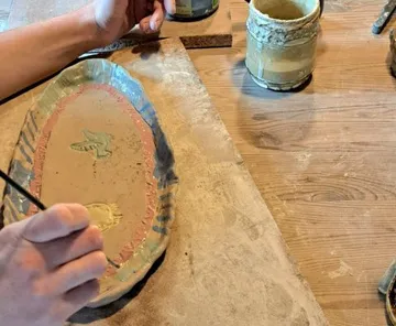 Hand paint a ceramic bowl on a wooden surface with paints.