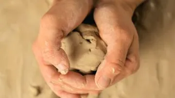 Hands form a lump of clay on a surface.