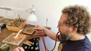 Ein Mann nutzt eine Lötlampe an einem Werkstatttisch.