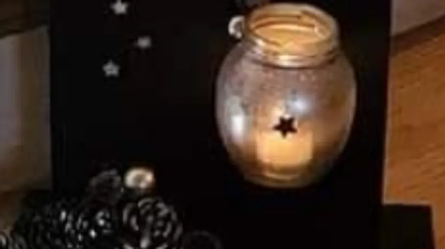 Lit candle in star-patterned jar decor.