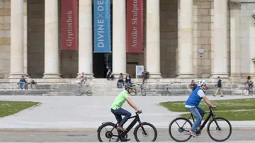 Zwei Radfahrer fahren vor einem Museum mit Säulen.