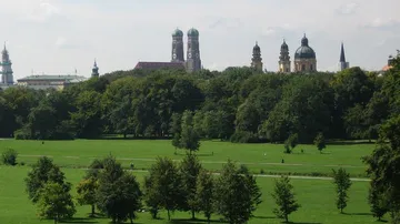Bäume stehen in einem Park mit Kirchen im Hintergrund.