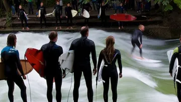 Surfer reitet auf einer Welle, Zuschauer am Ufer beobachten.