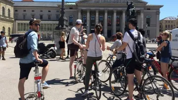 Cyclists stand in front of an impressive historic building.