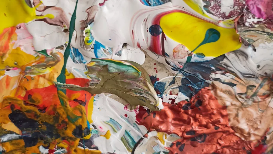 Colourful blobs of paint mix on a textured surface.