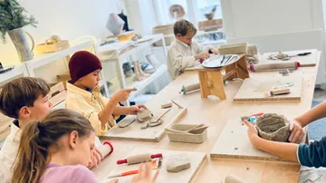 Kinder formen mit Ton an einem Tisch in einem Atelier.