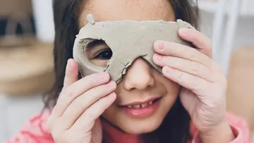 Ein Mädchen hält eine Maske aus Ton vor ihrem Gesicht.