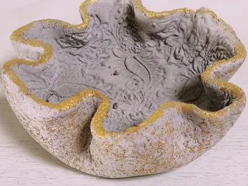 Concrete bowl with golden decoration, on a bright table.