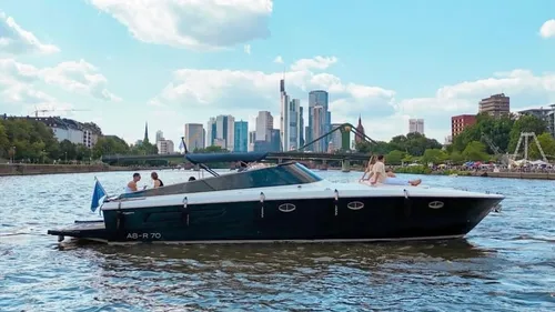 A boat sails on a river in front of an urban landscape.