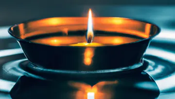 A flaming candle floats in a metal bowl.