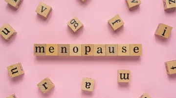Holzbuchstaben bilden das Wort „menopause“ auf rosa Hintergrund.