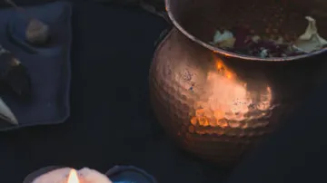 Kupferne Schüssel mit Blumen, Kerzen in dunkler Umgebung.