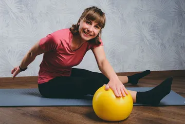 Frau dehnt sich mit einem gelben Ball auf einer Matte.