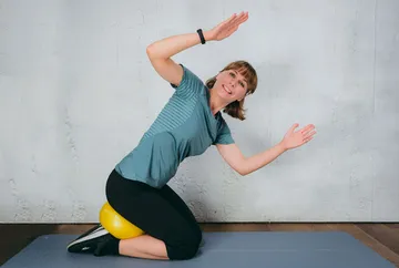 Eine Person balanciert auf einem Gymnastikball im Raum.