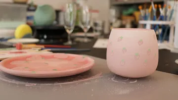 Rosa Tasse und Teller mit Erdbeer-Muster auf Tisch.