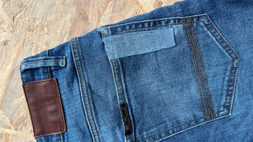 Jeans mit beschädigter Tasche auf Holzuntergrund.