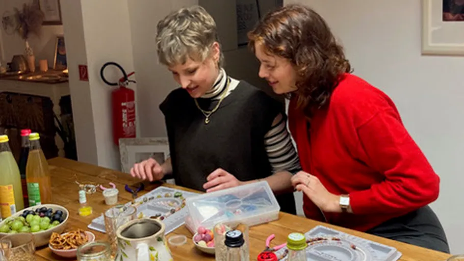 Two women look at colorful objects on a table together.
