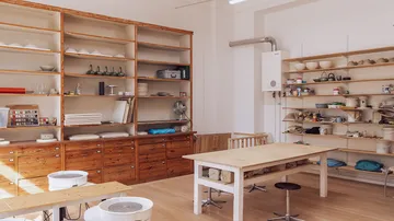 Töpferwerkstatt mit Regalen, Töpfen und einem Arbeitstisch.
