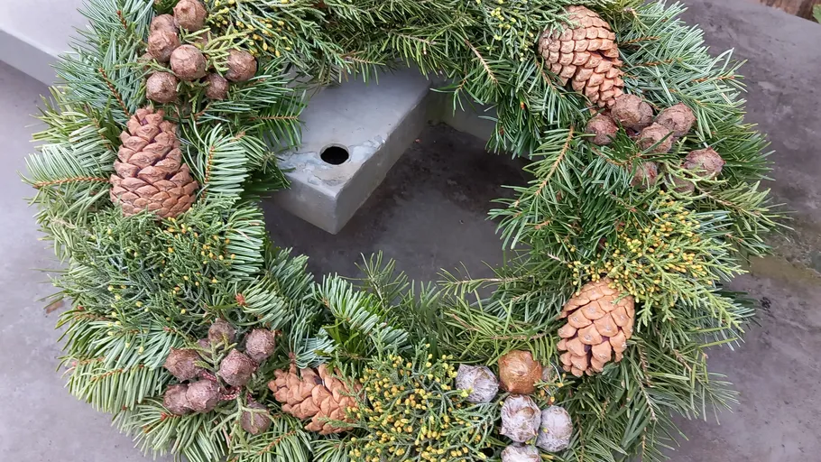 Pine cone wreath with greenery on table.