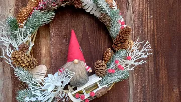 A wreath with pine cones and a red gnome.