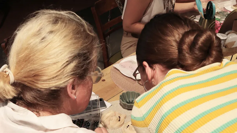 Two women curiously observe an object on the table.