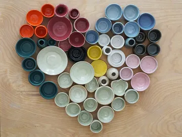Colourful bowls form a heart-shaped pattern on wood.