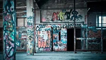 Verlassene Halle mit farbenfrohen Graffiti und einer Tür.