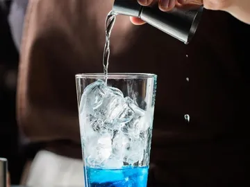 Glas mit Eis wird mit klarem Getränk gefüllt.