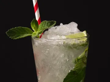 Ein Glas Cocktail mit Eis, Minze und Strohhalm.