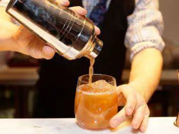 Barkeeper schüttet Getränk in ein Glas voller Eis.