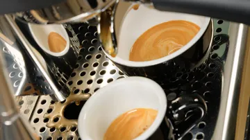 Glossy Kaffeemaschine brüht Espresso in schwarze Tassen auf.