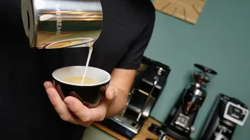 Eine Person gießt Milch in eine Kaffeetasse.