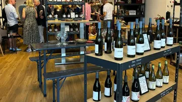 Tische mit Weinflaschen, Menschen diskutieren in einem Weinladen.