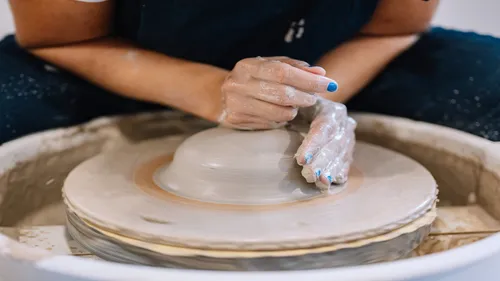 Pottery wheel shapes clay with hands in workshop.