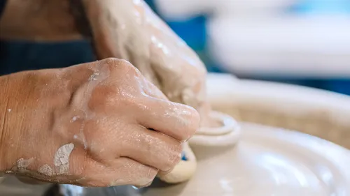 Hands form clay on a potter's wheel in a studio.