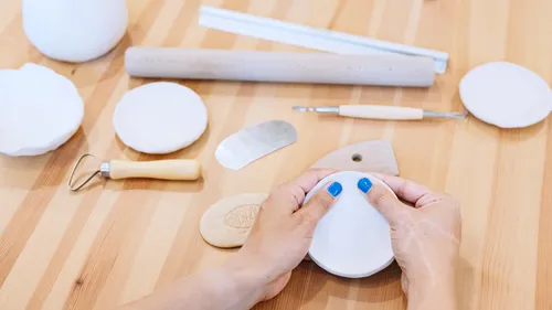 Hands form a white clay circle on a wooden table.