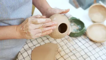 Hände formen einen Tontopf auf einem Tisch.