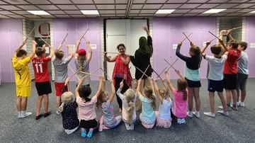 Children hold sticks, dance around the room under guidance.